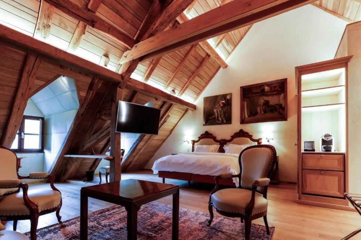 Une chambre avec un plafond en pente, un lit, une télévision et des œuvres d’art accrochées au mur.
