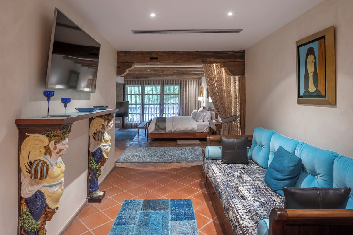Une chambre d’hôtel avec un lit, un canapé, une télévision, une sculpture en bois et un tableau au mur.