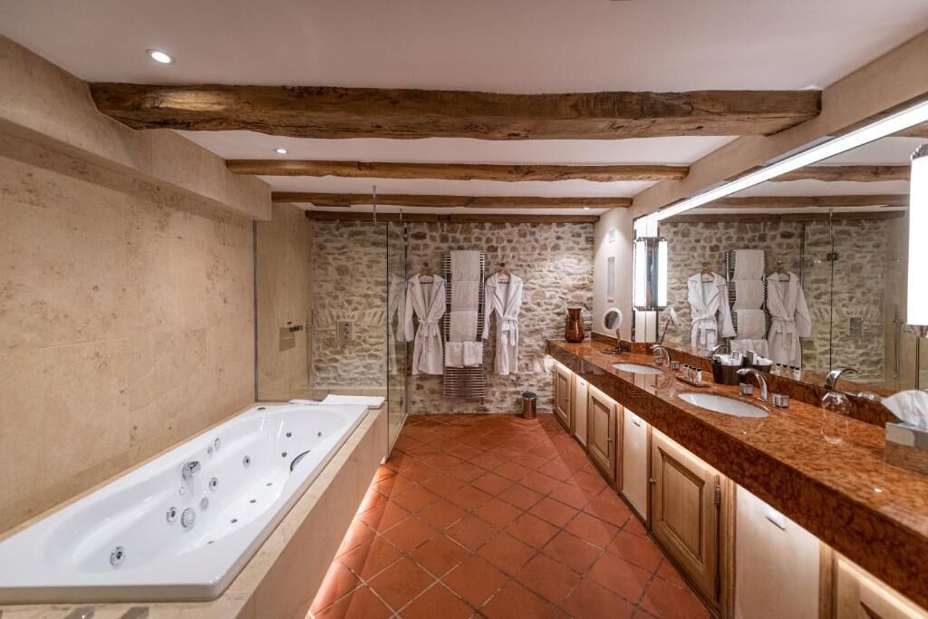 A modern bathroom with a stone wall, a large bathtub, and a vanity with two sinks.