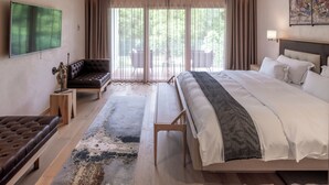 A modern hotel room with a large bed, a sofa, a TV, and a balcony with a view of trees. - Auberge Saint Walfrid  (Sarreguemines)