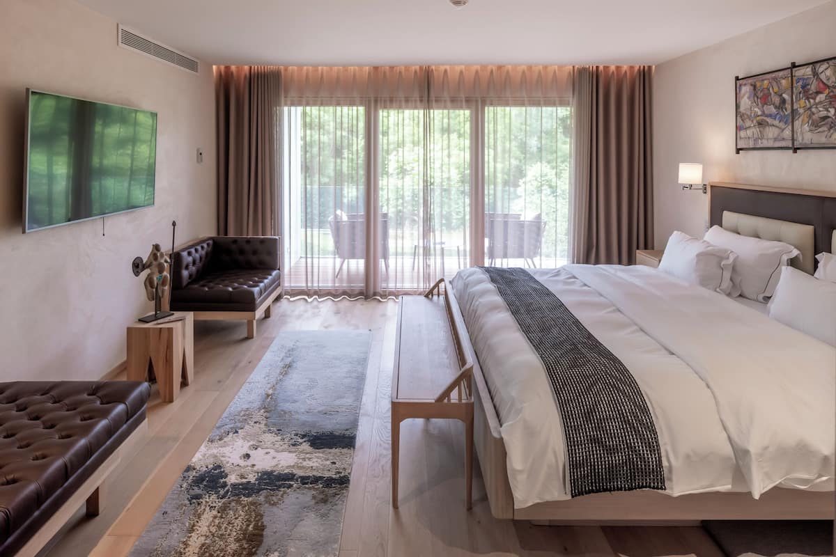 Une chambre d’hôtel moderne dotée d’un grand lit, d’un canapé, d’une télévision et d’un balcon offrant une vue sur les arbres.