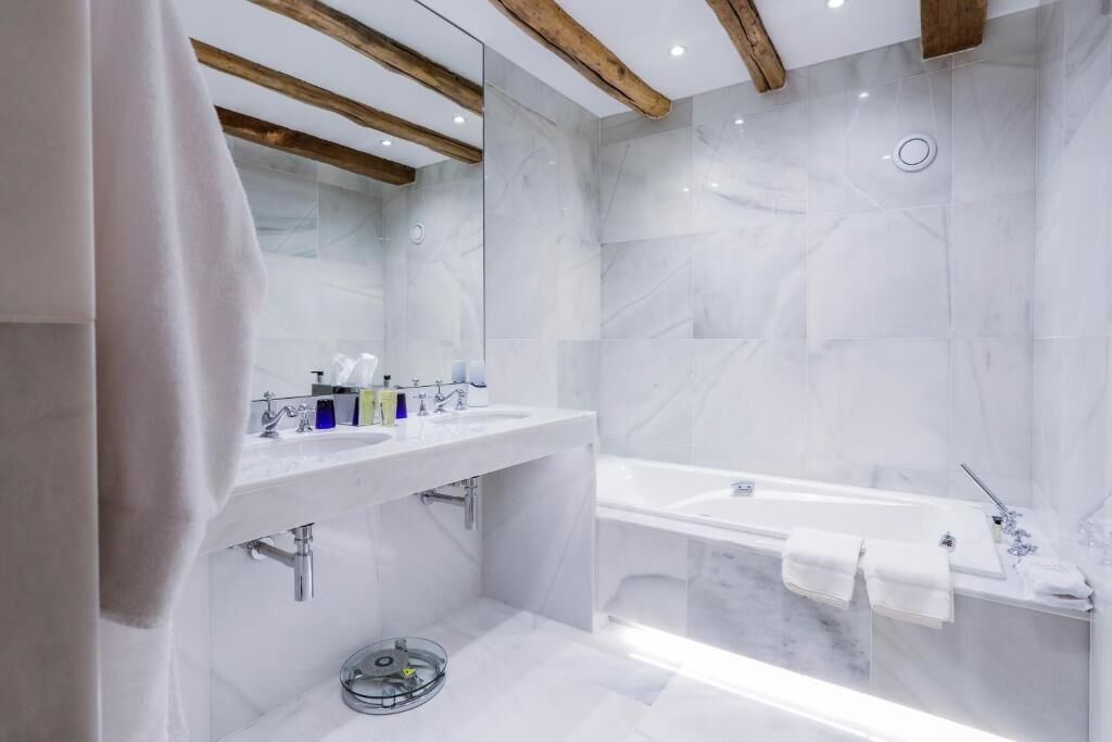 A modern bathroom with a marble sink, a bathtub, and wooden beams on the ceiling.