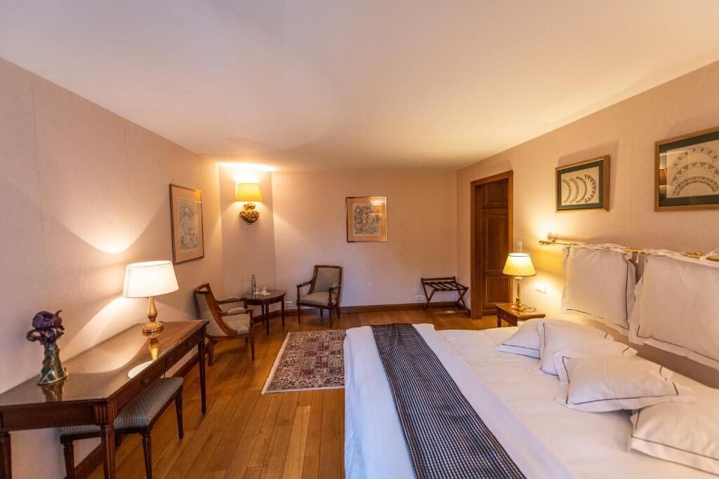 Habitación de hotel con cama, mesitas de noche, lámparas, escritorio, sillas e imágenes enmarcadas en las paredes.