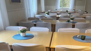 A hotel dining area with multiple tables and chairs, each with a blue placemat and a small vase of flowers. - Traume Vandrarhem (Visby)
