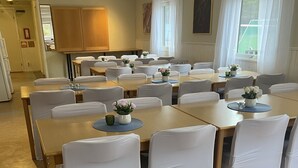 A conference room with multiple tables and chairs, white tablecloths, and small flower arrangements. - Traume Vandrarhem (Visby)