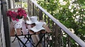 Un balcón con una mesa y sillas de madera, una planta en maceta y un cojín rojo.