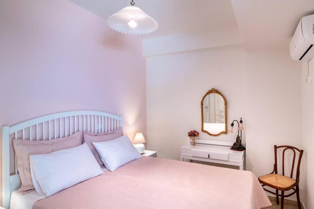 A bedroom with a bed, a nightstand, a dresser, a chair, a mirror, and an air conditioning unit.