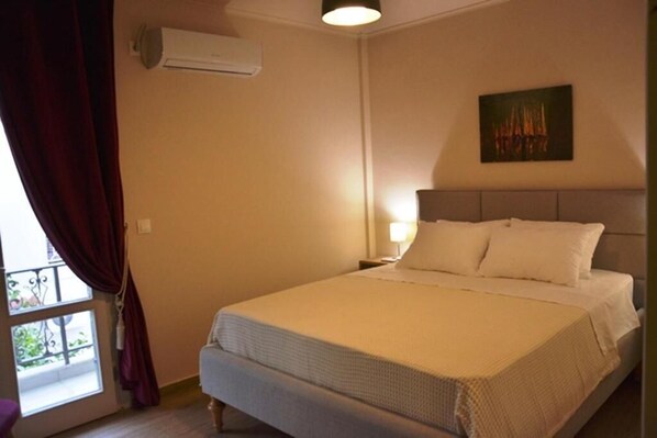 A bedroom with a bed, a nightstand, a painting on the wall, and an air conditioning unit. - Contessa Elli Residences (Kefalonia)