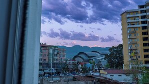 A cityscape with a prominent curved building in the center, surrounded by multi-story residential buildings and a mountain range in the background. - Cozy & Stylish Suite room with a Garden view in Batumi (BATUMI)