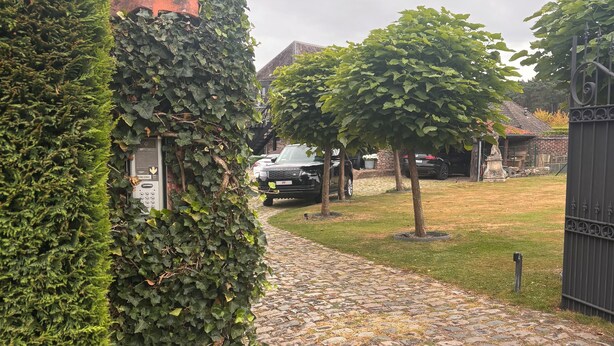 Ein Kopfsteinpflasterweg führt zu einem befestigten Bereich, in dessen Nähe ein Auto geparkt ist.