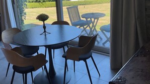 Ein Essbereich mit einem runden Tisch, vier Stühlen, einer kleinen Topfpflanze und Blick auf einen Garten und ein Haus durch große Glasschwingtüren.