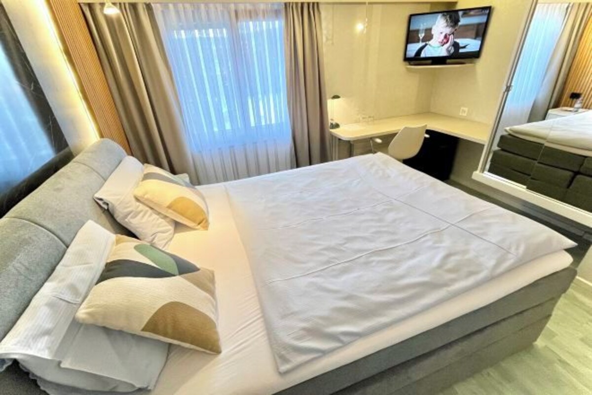 A hotel room with a bed, a desk, a TV, and a window with curtains.