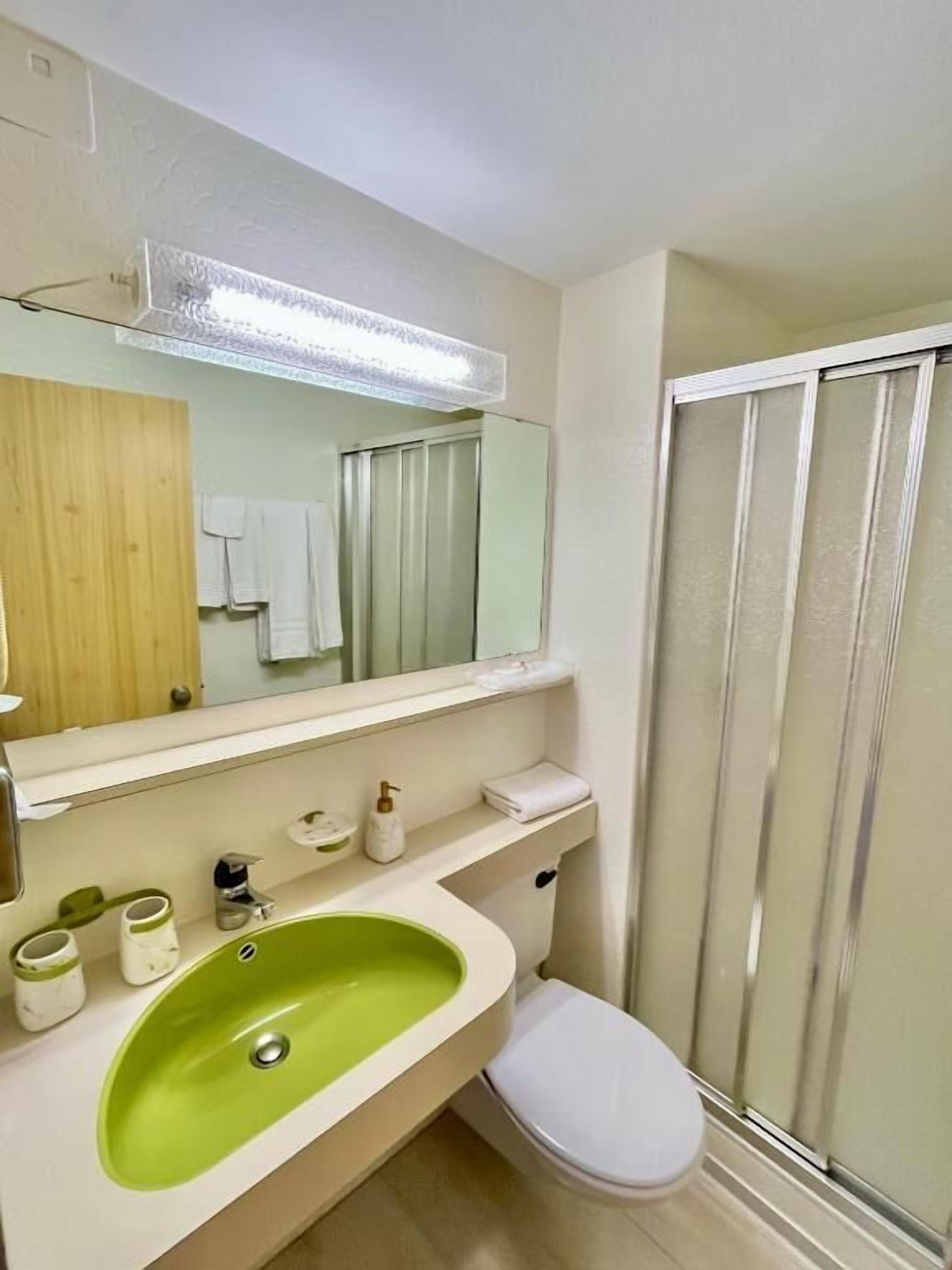 Een badkamer met een groen wastafel, een wit toilet en een douchecabine.