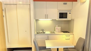Un angolo cottura compatto con forno a microonde, lavello e bollitore elettrico. È presente un piccolo tavolo da pranzo con due sedie.