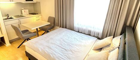 A hotel room with a bed, a desk, a chair, a microwave, and a window with curtains.