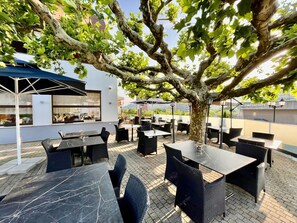 An outdoor patio with tables and chairs, surrounded by trees and a building with windows. - Seilers Hotel (Liestal)