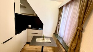 Una cucina compatta con un tavolo da pranzo e una sedia, una piccola pianta sul tavolo e una finestra con tende.