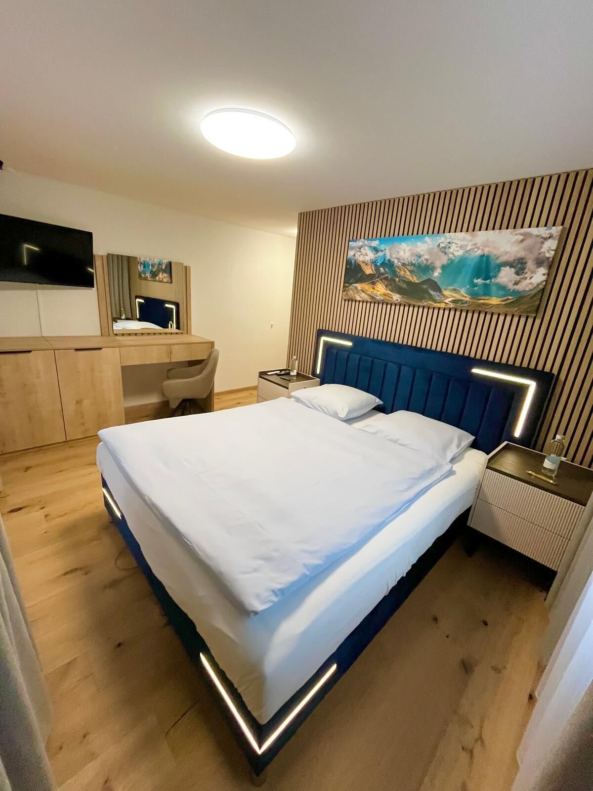 Une chambre d’hôtel moderne, équipée d’un lit, d’un bureau, d’une chaise, d’une télévision et ornée d’un tableau au mur.