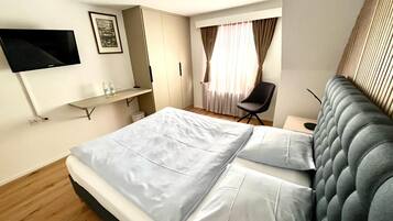 A modern hotel room with a bed, a desk, a chair, and a TV mounted on the wall.