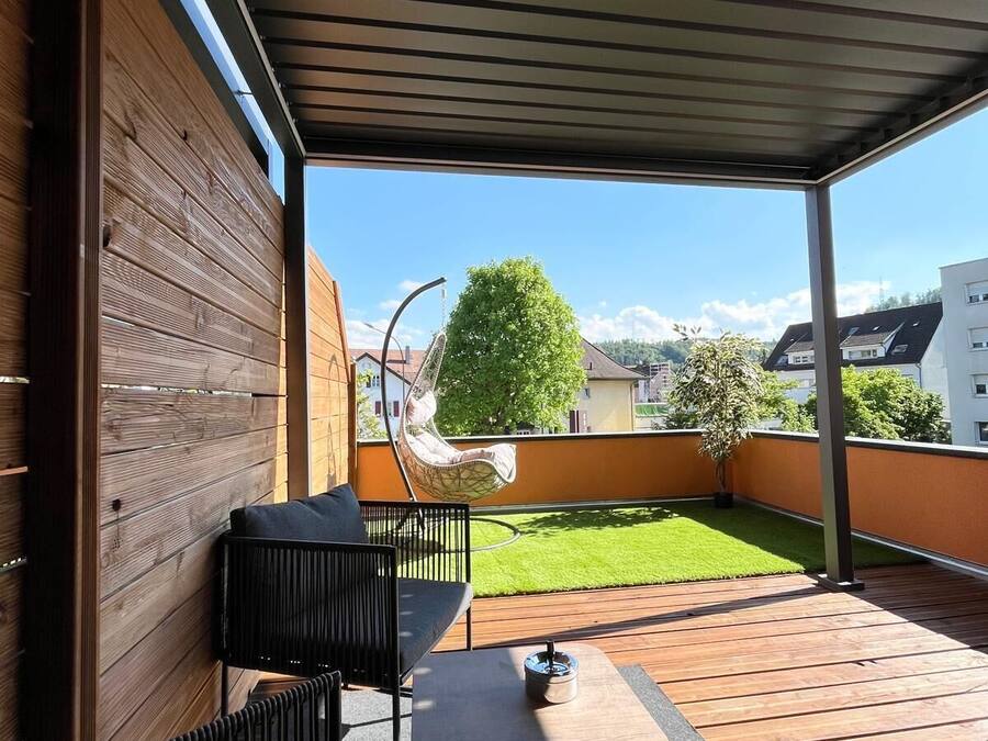 A covered outdoor patio with a wooden deck, a hanging chair, and a table.