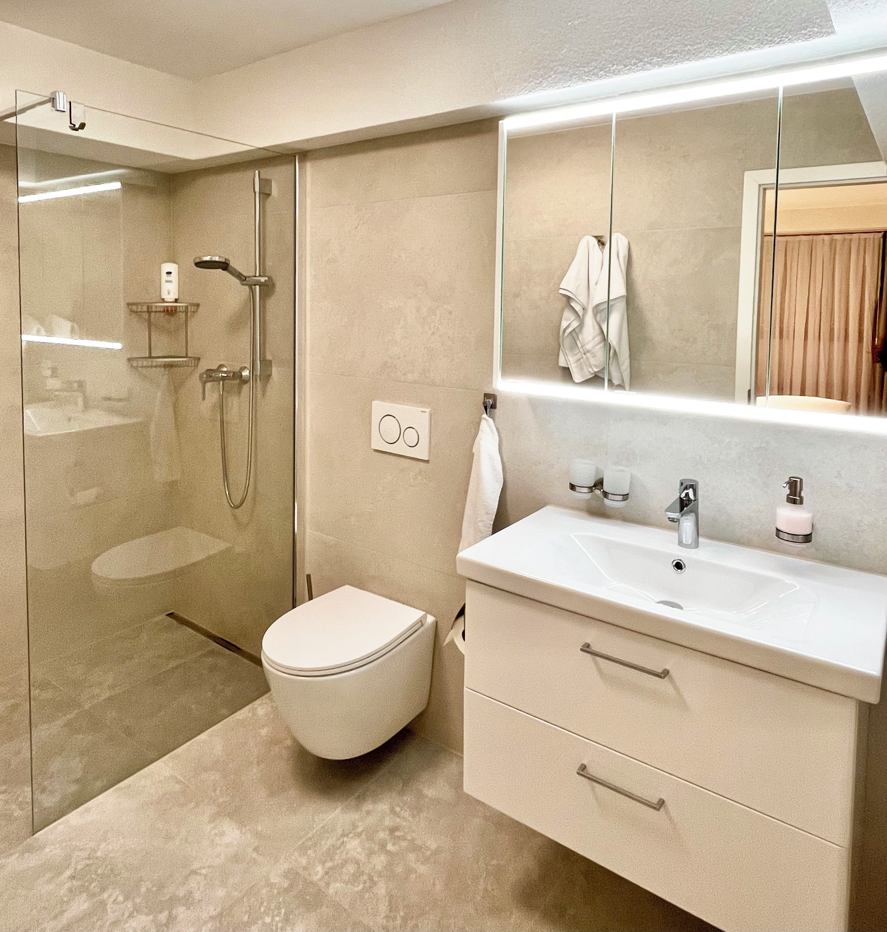 Un baño moderno con cabina de ducha de vidrio, inodoro, tocador con espejo y toallero.
