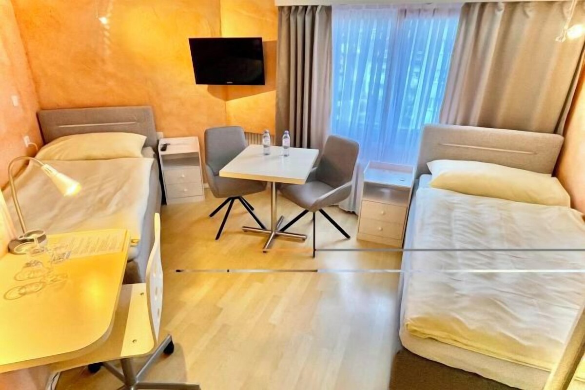 A hotel room with two beds, a desk with a chair, a TV, and a window with curtains.