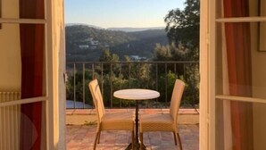 Un balcon ouvert avec une table et des chaises, offrant une vue sur un paysage vallonné.