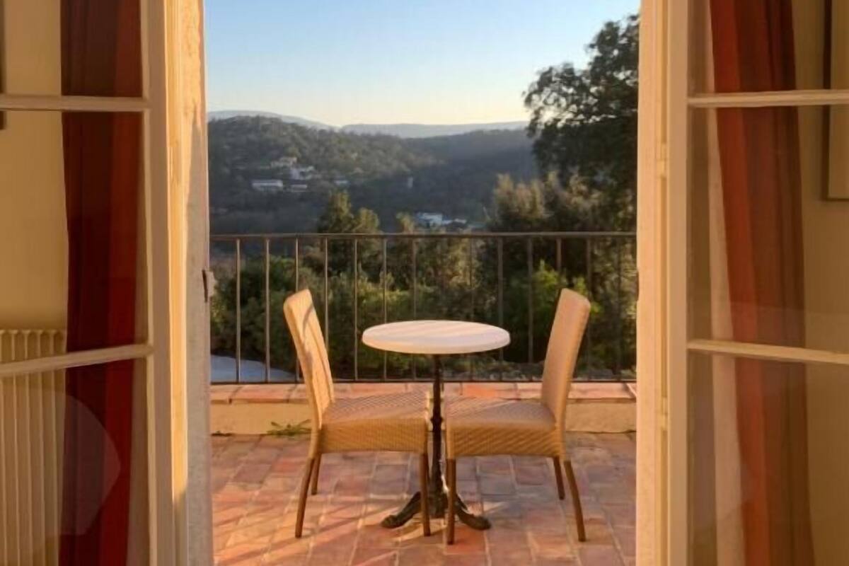 Un balcon ouvert avec une table et des chaises, offrant une vue sur un paysage vallonné.