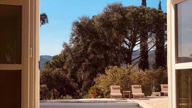 Une vue sur une piscine, avec des chaises longues et un pot de fleurs, le tout encadré par un cadre de porte.