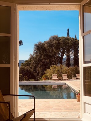 Vista de una piscina con sillas de descanso y una planta en maceta, enmarcada por un arco.