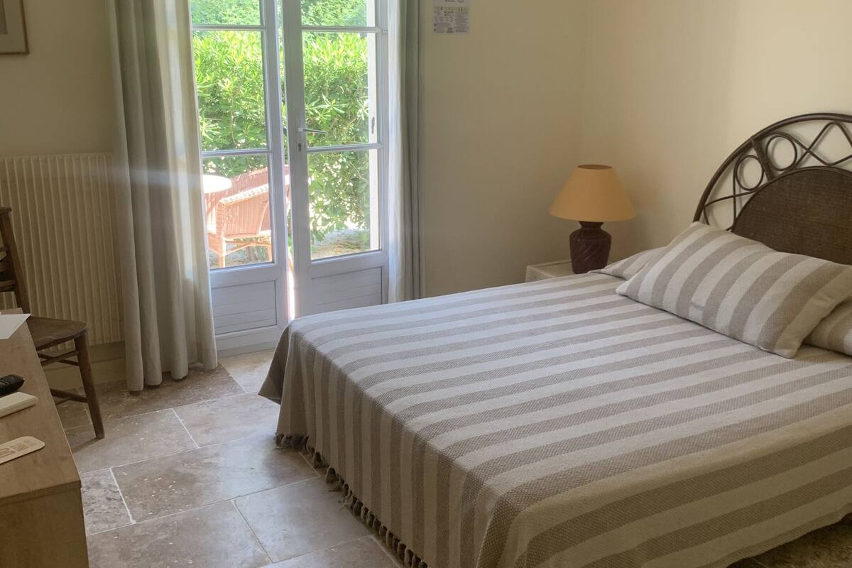 Une chambre avec un lit, un bureau, une lampe et une vue sur la verdure.