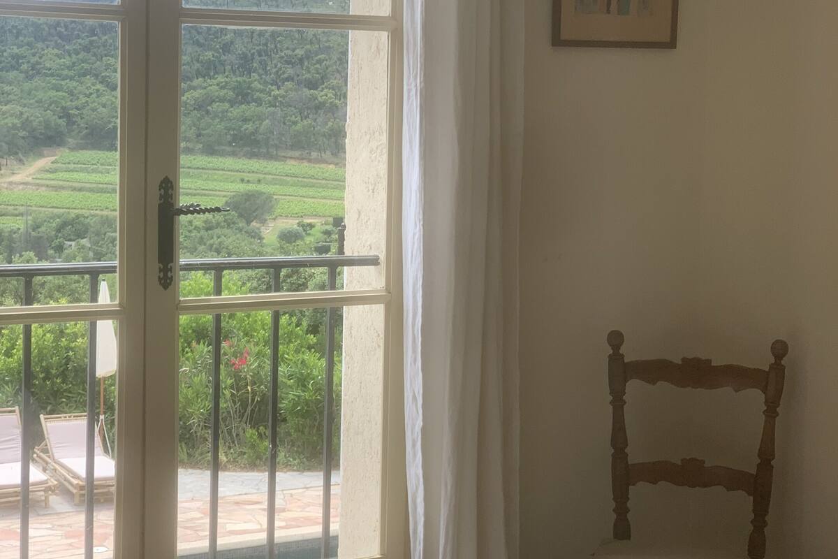 Une chambre avec un lit, une chaise, un tableau et un balcon donnant sur un paysage verdoyant.