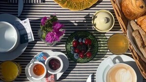 Une table de petit-déjeuner avec des croissants, des fruits, du café et des condiments, le tout disposé sur une nappe à rayures.