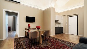 A modern living room with a glass dining table, two chairs, a red decorative bowl, a flat-screen TV on the wall, and a patterned rug. - Archimedes suites  (Catania)