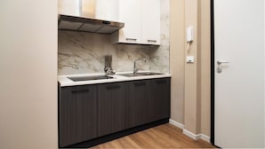 A compact kitchen with dark cabinets, a marble backsplash, and a single sink. - Archimedes suites  (Catania)