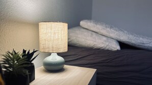 A bedside table with a lamp, a small potted plant, and a neatly made bed with pillows. - Cozy Flats Silkeborg - S3 (Silkeborg)