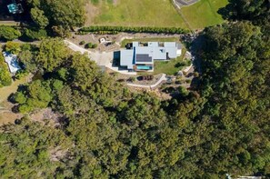 Vue aérienne d’une maison moderne dotée d’une piscine, entourée d’une forêt dense.