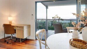 A modern room with a wooden desk, a white chair, a round table, and a view through large glass windows. - Cooinda Luxury Residence and Studio (Valdora)