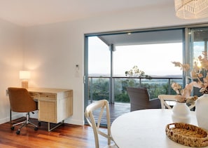 Une chambre moderne avec un bureau en bois, une chaise blanche, une table ronde et une vue dégagée grâce à de grandes fenêtres en verre.
