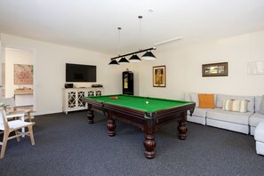 Een kamer met een pooltafel, een bank, een televisie en een kast.