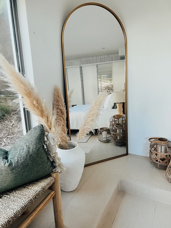 A modern bedroom with a large mirror, a bed, and decorative plants.