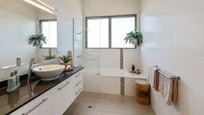 A modern bathroom with a large sink, a bathtub, and a window.
