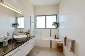 A modern bathroom with a large sink, a bathtub, and a window.