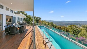 A modern outdoor deck with a pool, dining area, and a scenic view of the landscape.