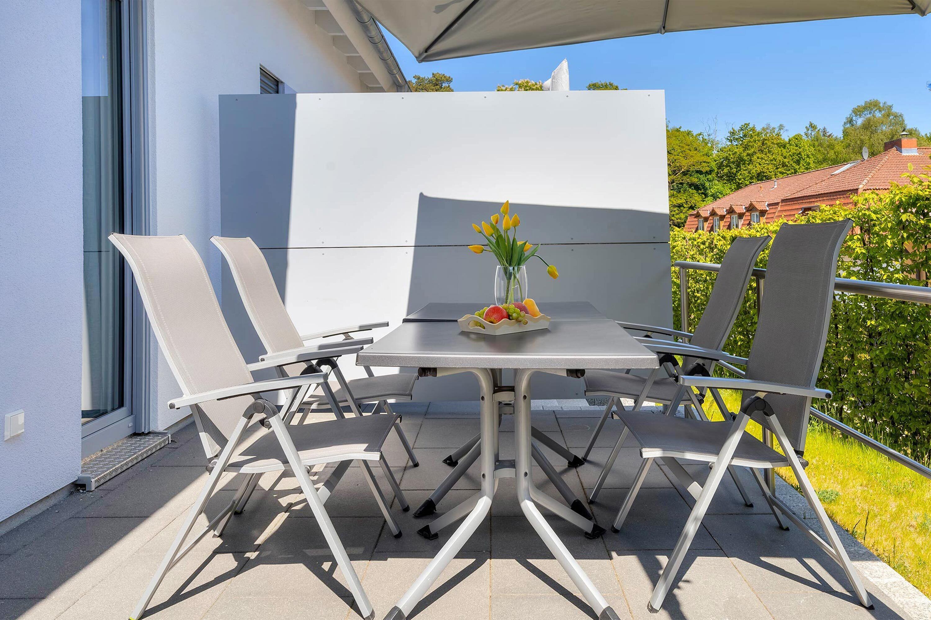 Une terrasse extérieure avec une table et des chaises, un vase rempli de fleurs et un panier de fruits.
