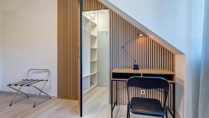 Een kleine kamer met een bureau, stoel en een kledingroede.