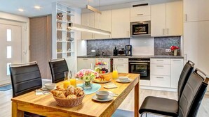 Een moderne keuken met witte kasten, een marmeren aanrechtblad en een eethoek met een houten tafel en stoelen.