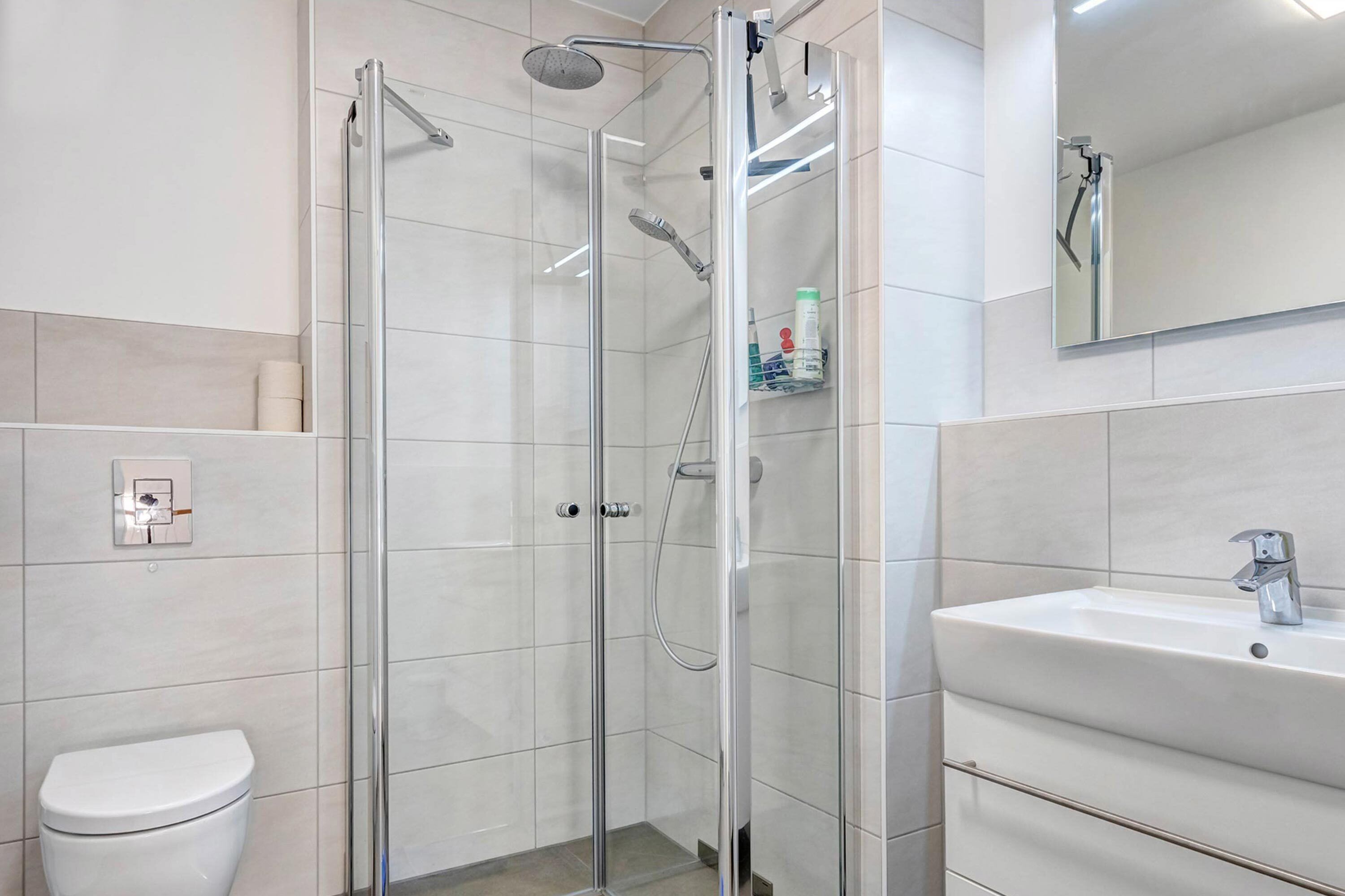 Een moderne badkamer met een douchecabine van glas, een wit toilet en een wastafel met spiegel erboven.