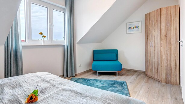 Een slaapkamer met een bed, een blauwe bank, een houten kledingkast en een raam met gordijnen.