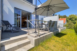 A modern outdoor patio with a covered seating area, a glass door entrance, and a stone staircase leading to the entrance. - Vacation home Nordhorn - your cozy home in Koserow on the Baltic Sea (Ostseebad Kölpinsee)